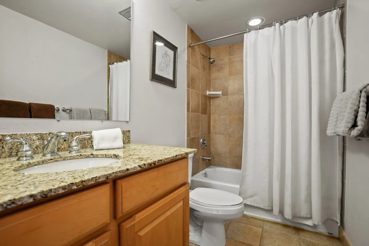 A stylish full bathroom with a granite countertop, a walk-in shower area, and a framed mirror. The lighting is soft and the space feels refreshing and serene, perfect for unwinding or preparing for the day ahead.