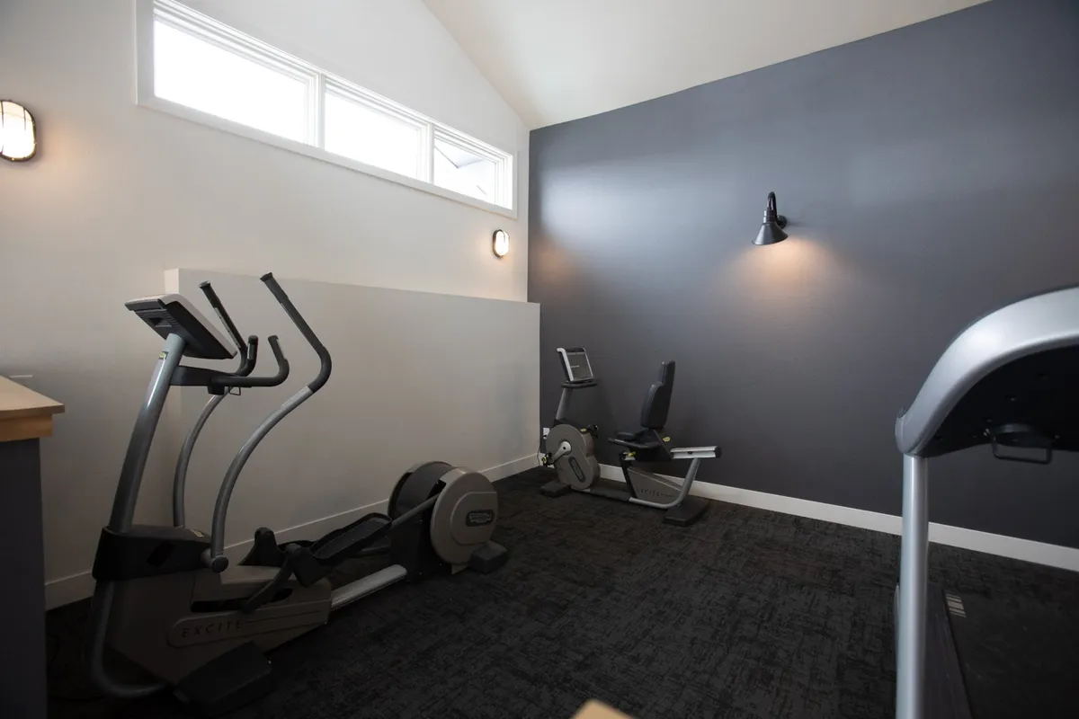 A bright, well-equipped fitness area featuring an elliptical machine and a stationary bike. The setting is clean, motivational, and suitable for personal wellness routines.