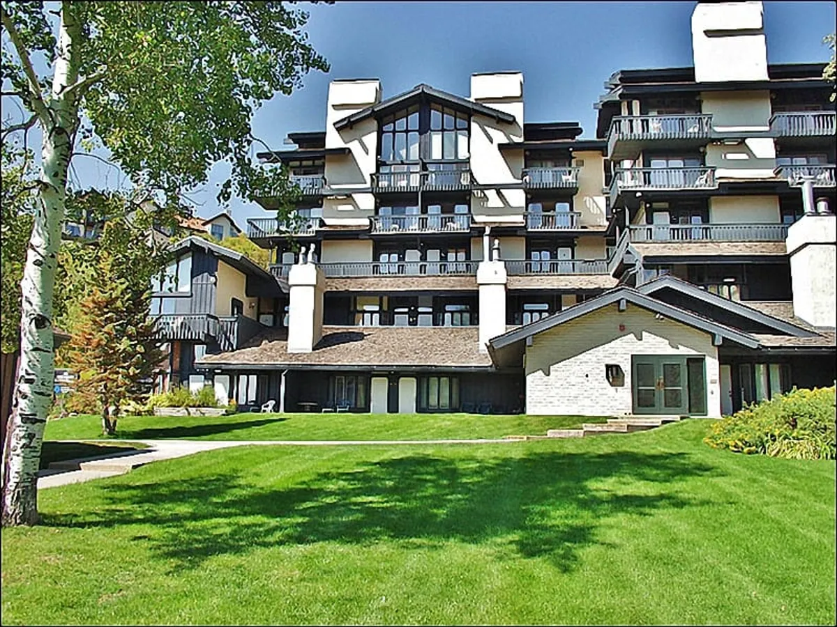 The hero image showcases a multi-level condo building set amidst a spacious, lush green lawn and framed by mature trees, with balconies facing a radiant sunset. The scene exudes tranquility, inviting guests to unwind outdoors or take in sweeping views from private balconies.