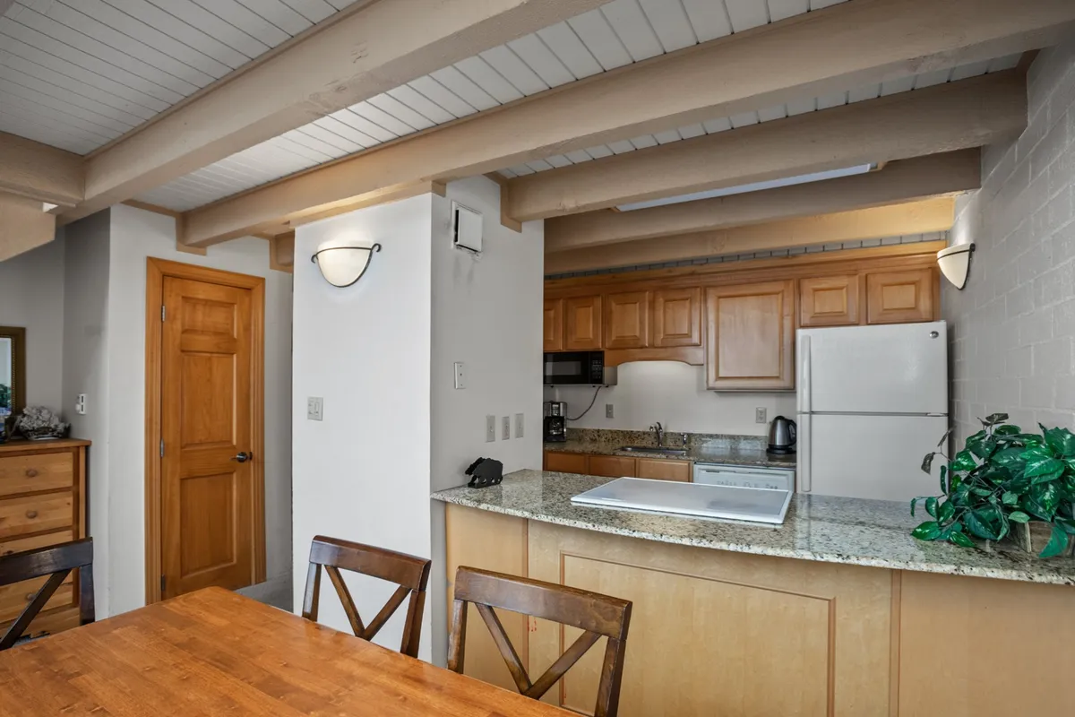 A cozy, inviting kitchen and dining space featuring a wooden dining table set against a backdrop of granite countertops, modern appliances, and warm wooden cabinetry. The kitchen is open to the living area, enabling easy conversation and plenty of natural light, while the dining area is perfect for both casual family breakfasts and festive dinners.