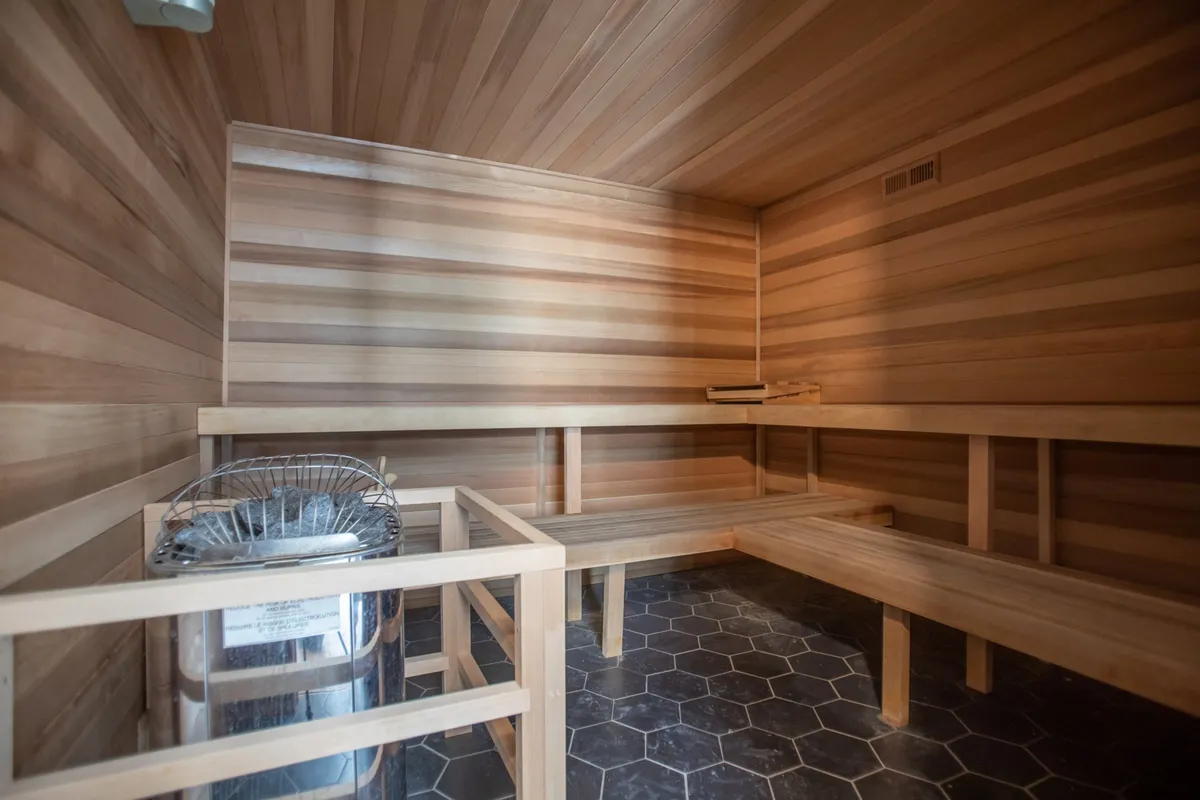A serene sauna interior with wooden benches and a sauna heater, complemented by hexagonal flooring. The calm atmosphere and thoughtful design create a space for relaxation and rejuvenation.