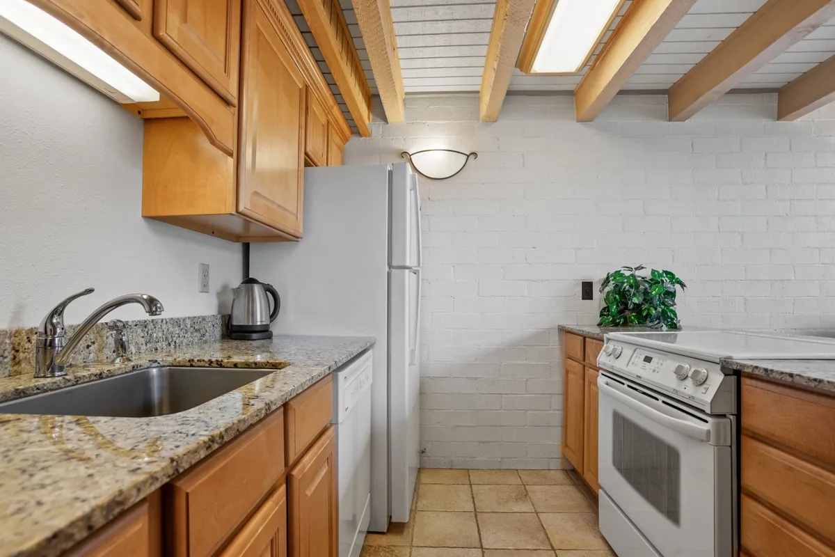 A welcoming kitchen with sleek granite countertops, modern appliances, and wooden cabinetry. The setting is bright and functional, with enough prep space for multiple people to cook together. A potted plant adds a touch of homeliness, reinforcing the kitchen as a social hub.