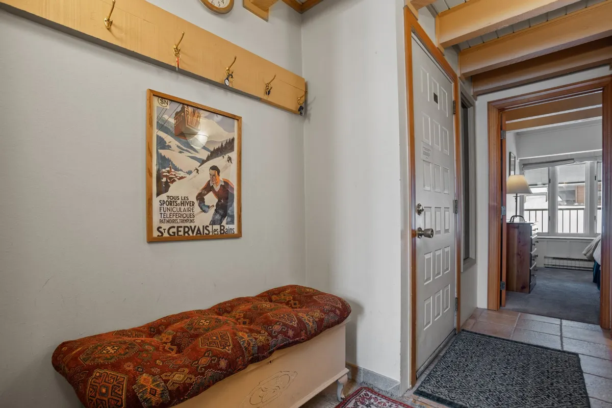 A welcoming entry nook with an ornate bench, vintage ski poster, and handy coat hooks, perfect for organizing winter gear or pausing before or after outdoor adventures. The area feels cozy and practical, setting the tone for a mountain getaway.