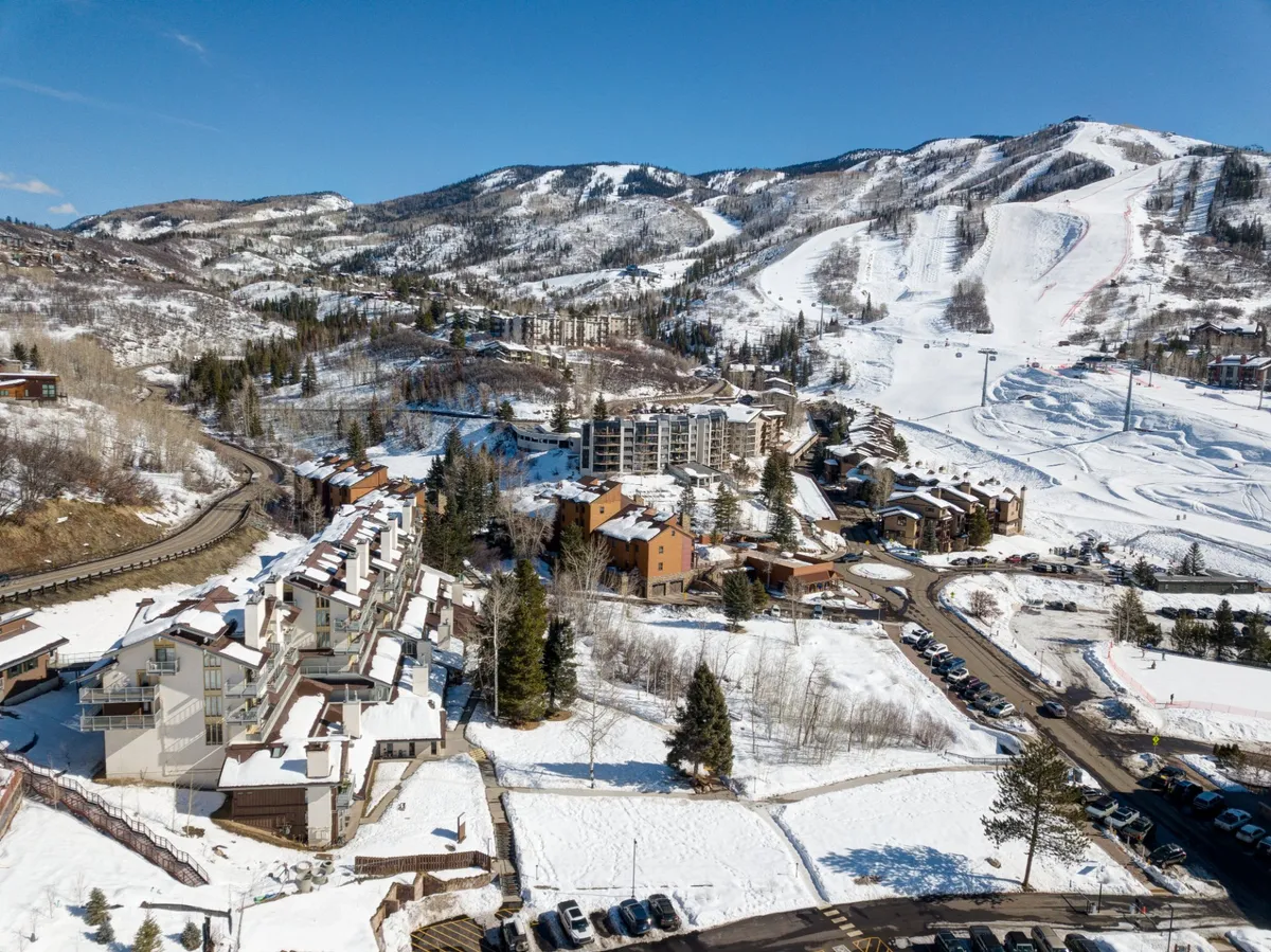 An exterior view of the Steamboat area, featuring snow-dusted mountains, ski slopes, residential buildings, pine trees, and access roads. The image evokes the sense of adventure and tranquility, representing the area's year-round appeal for hiking, biking, and community activities that draw guests during spring, summer, and fall.